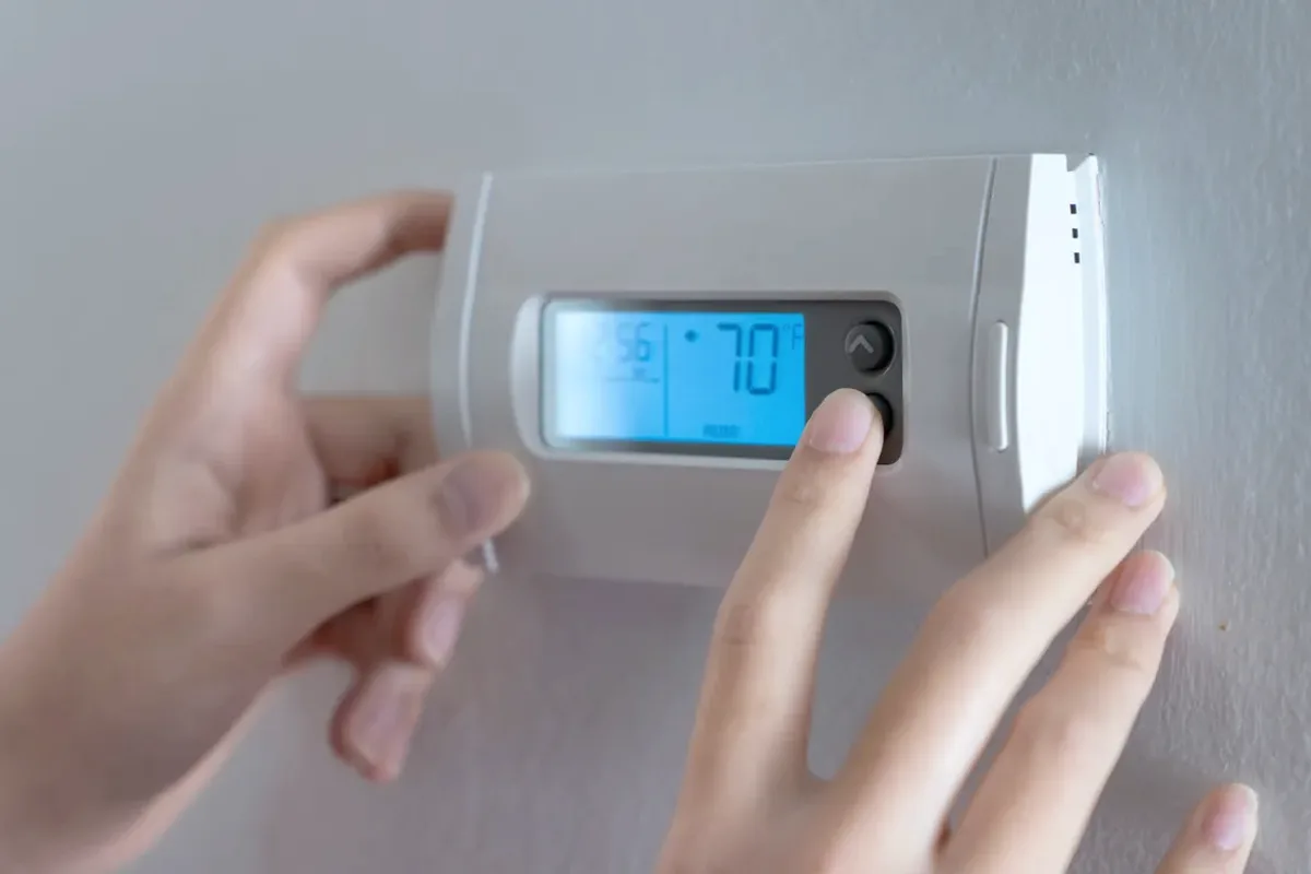 Hands adjusting a digital wall thermostat